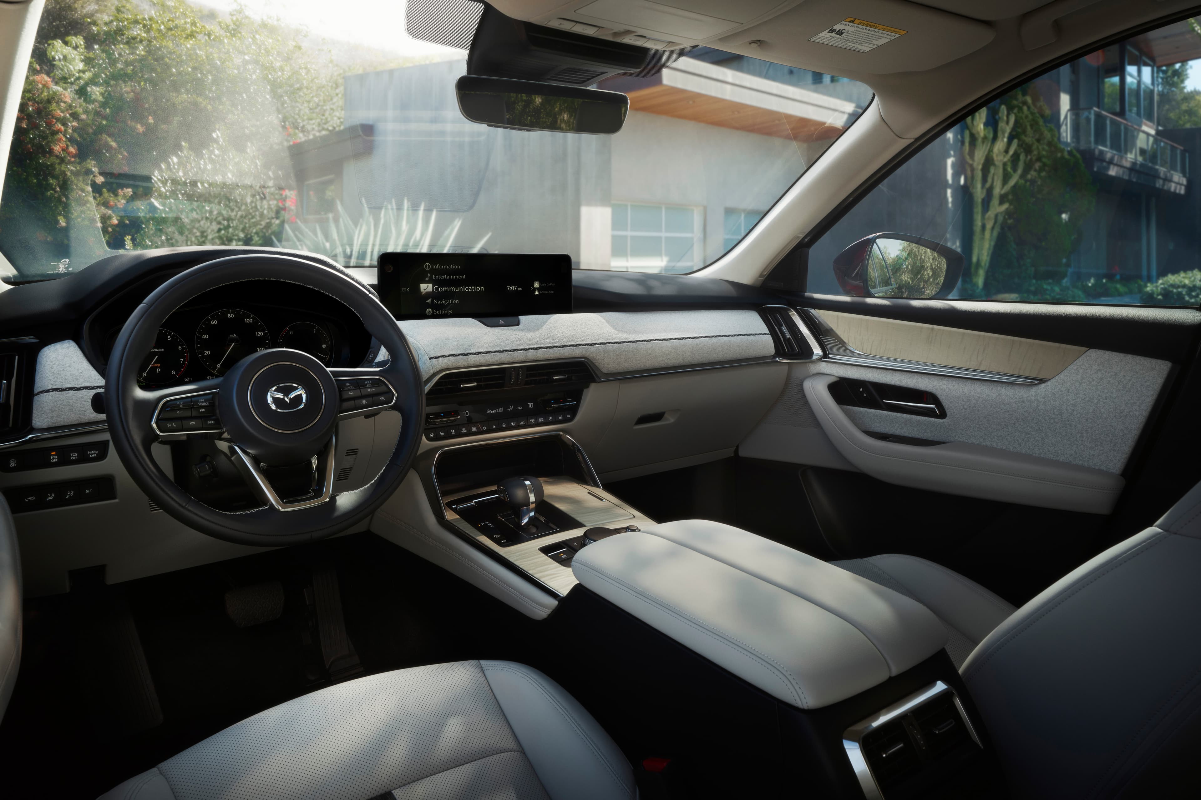 The Mazda CX-90 front cabin, with its widescreen centre display, pale leather seats and wood and cloth trim across the dashboard.