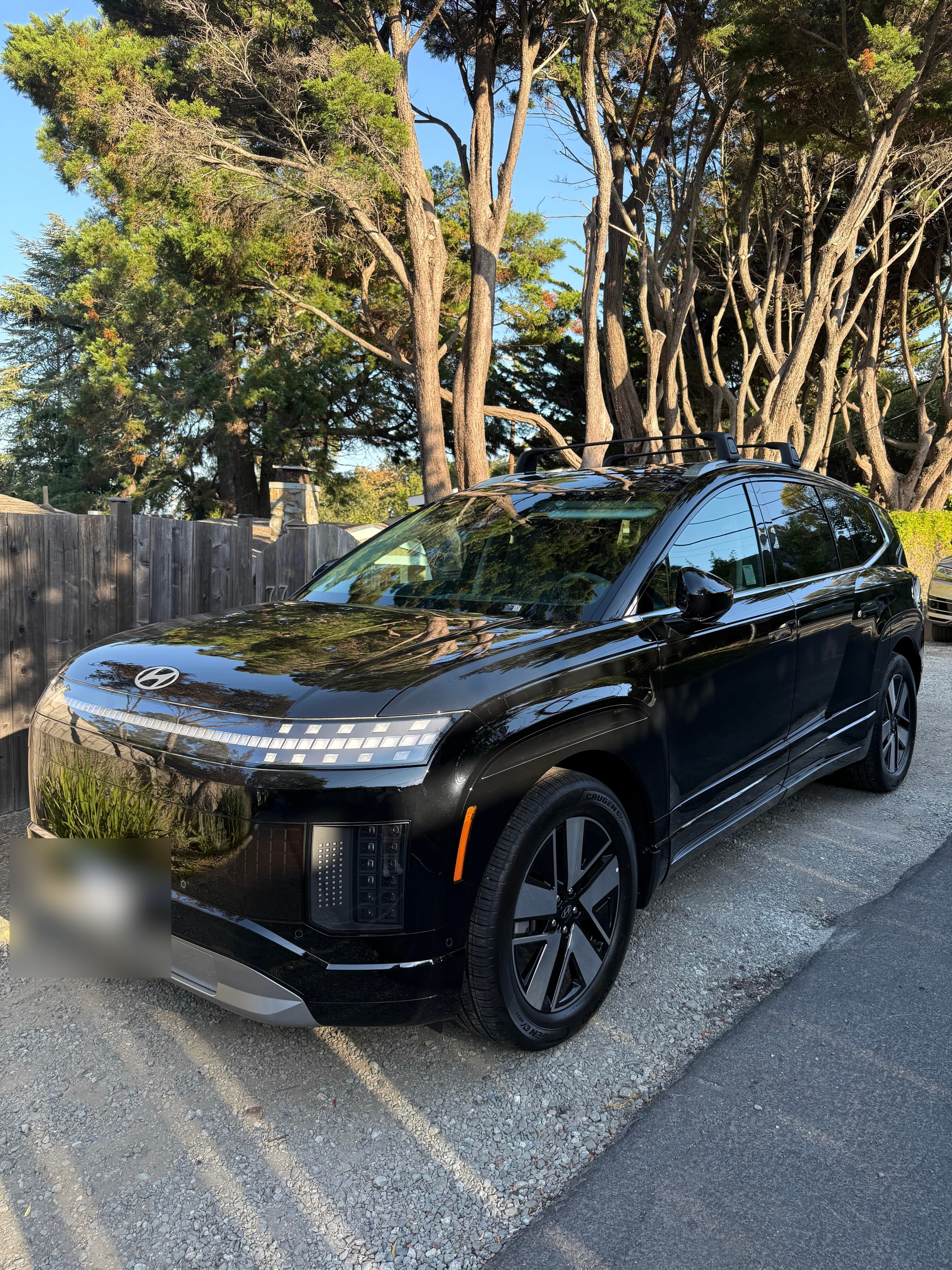 A black Hyundai IONIQ 9 on a gravel drive beneath Monterey cypress, delivered to a client