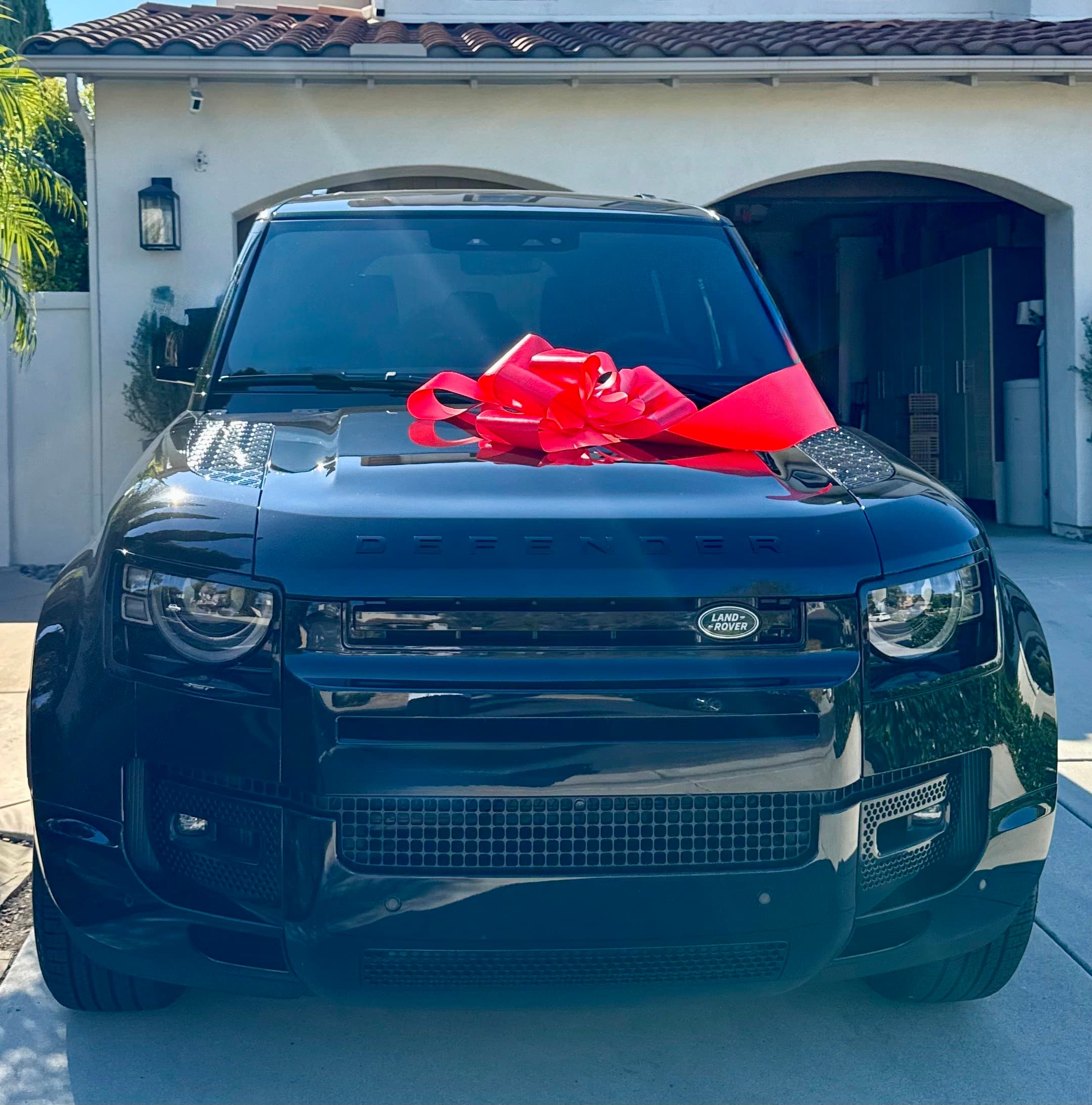 A Land Rover Defender with a delivery bow on a residential driveway