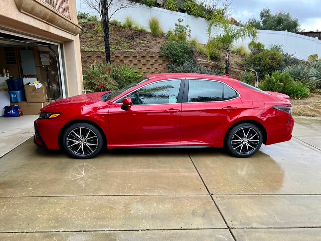 A red Toyota Camry parked on a residential driveway in front of an open garage