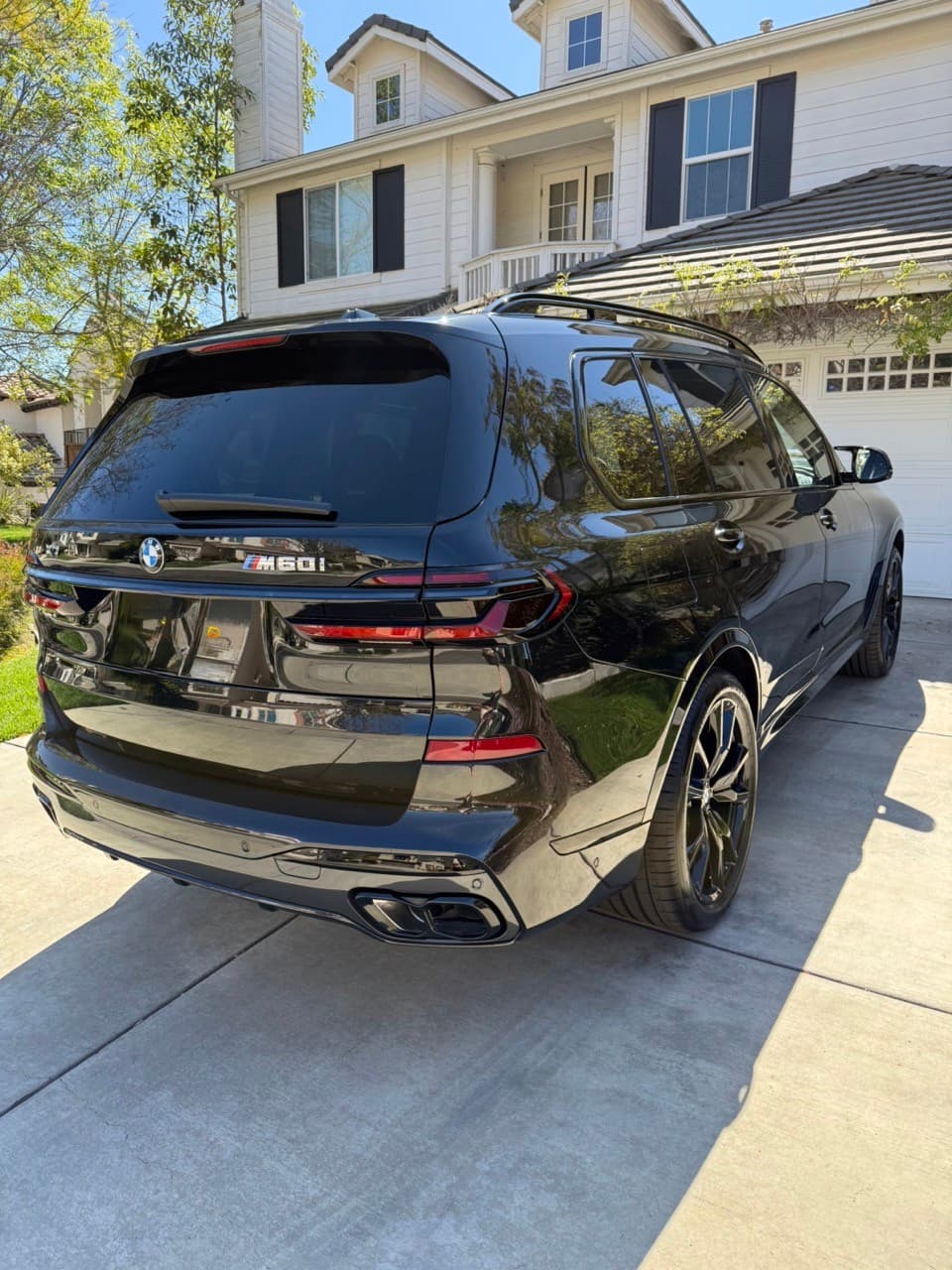 A black BMW X7 M60i in a client's driveway in front of a two-storey home, delivered in Los Angeles
