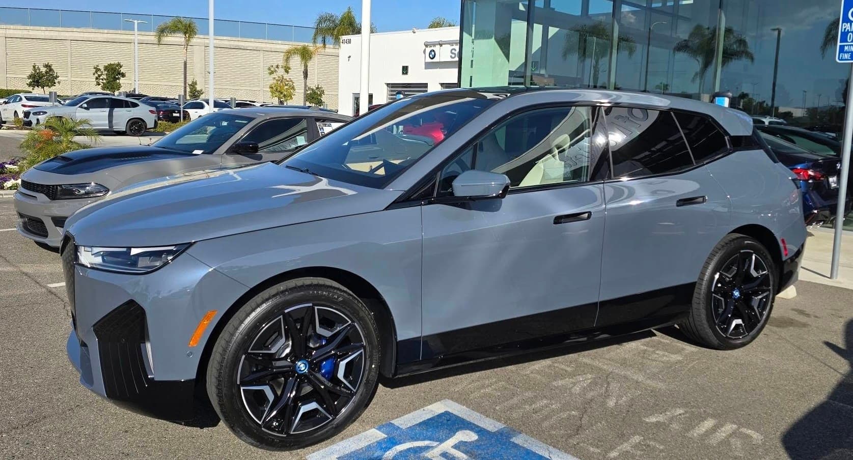 A grey BMW iX parked on a dealer lot, the used electric model the surrounding section works the numbers on.